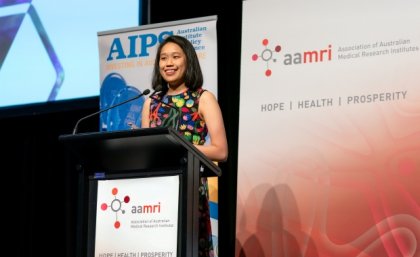 a woman stands at a lectern with banners behind her